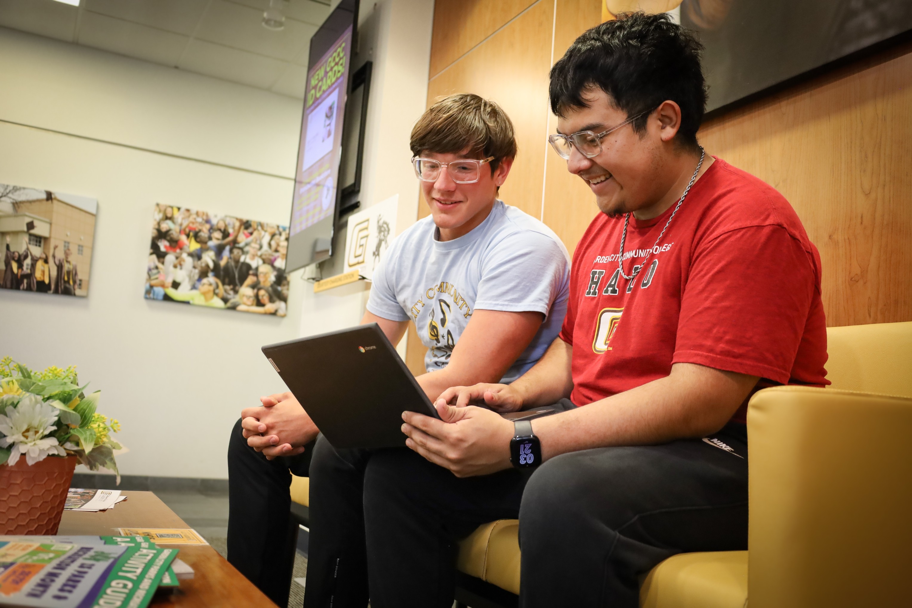 Two college students sit in a campus lounge reviewing information together on a laptop.