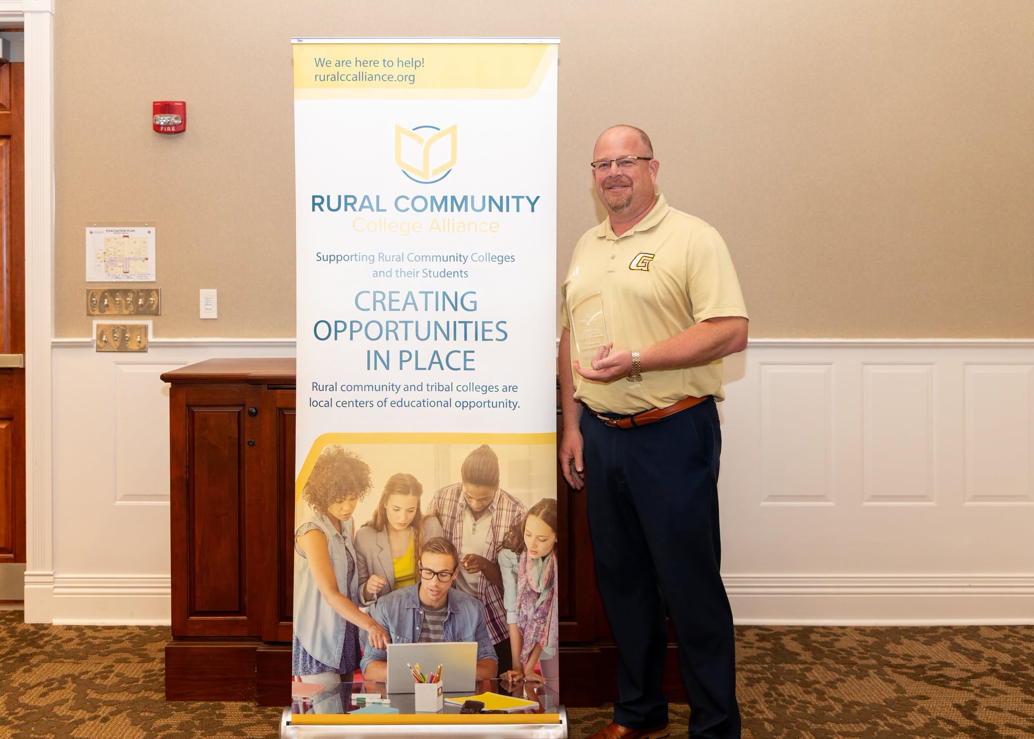 Man standing next to a banner promoting rural community colleges and educational opportunities in local places.