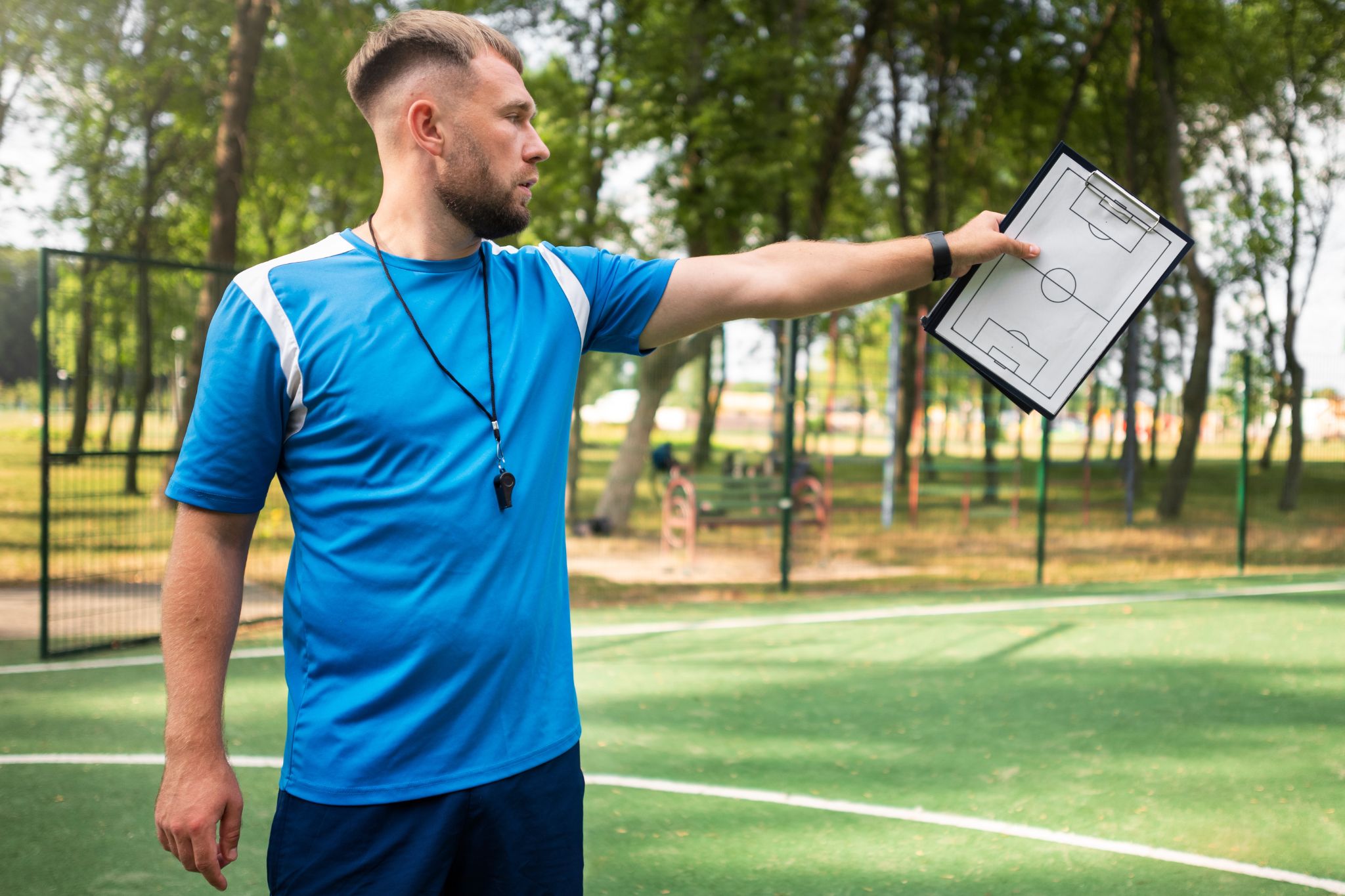 sports coach holding clipboard surrounded by field