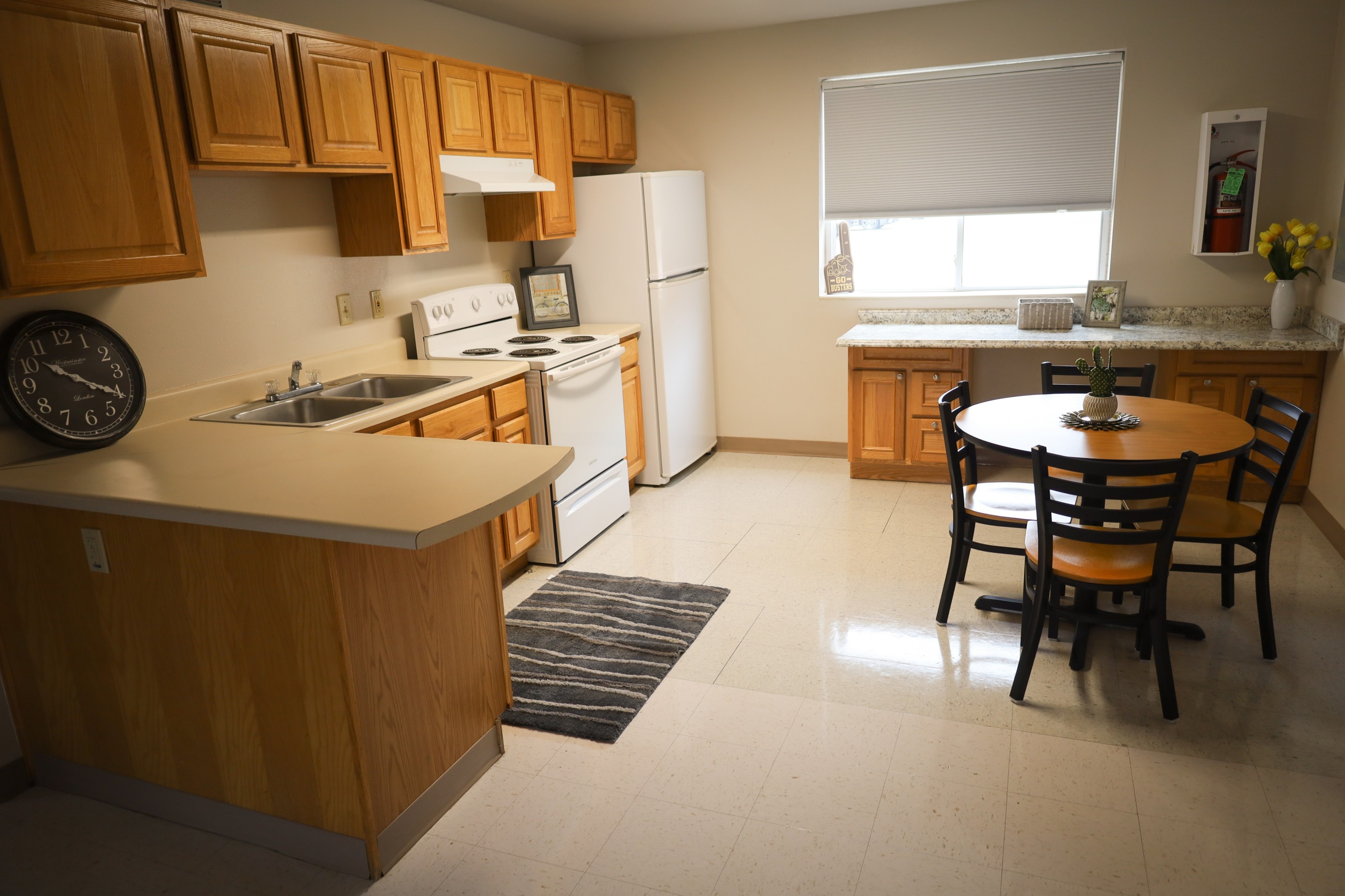 Kitchen with wooden cabinets, sink and stove, white refrigerator, and a small dining table with chairs near a window.
