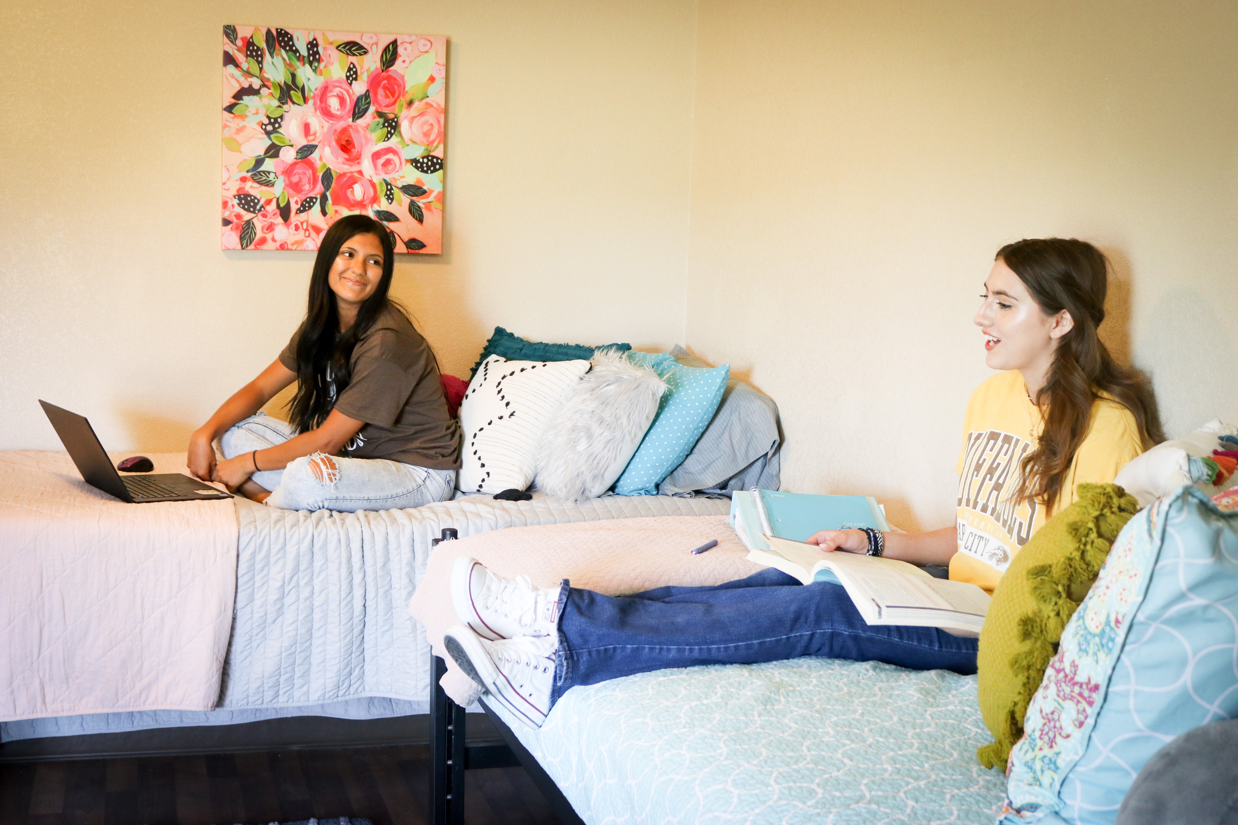Students studying and relaxing in a residence hall room with beds, books, and a laptop. Provide your feedback on BizChat